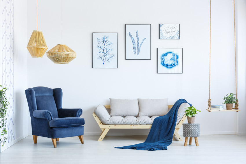 Sala de estar con silla acolchada azul, sofá, lámparas colgantes y elementos decorativos