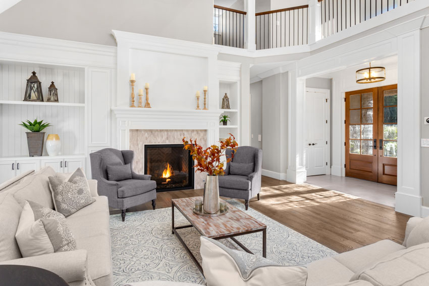 Sala de estar con sillas decorativas grises, sofá, alfombra, piso de madera, chimenea y puerta principal