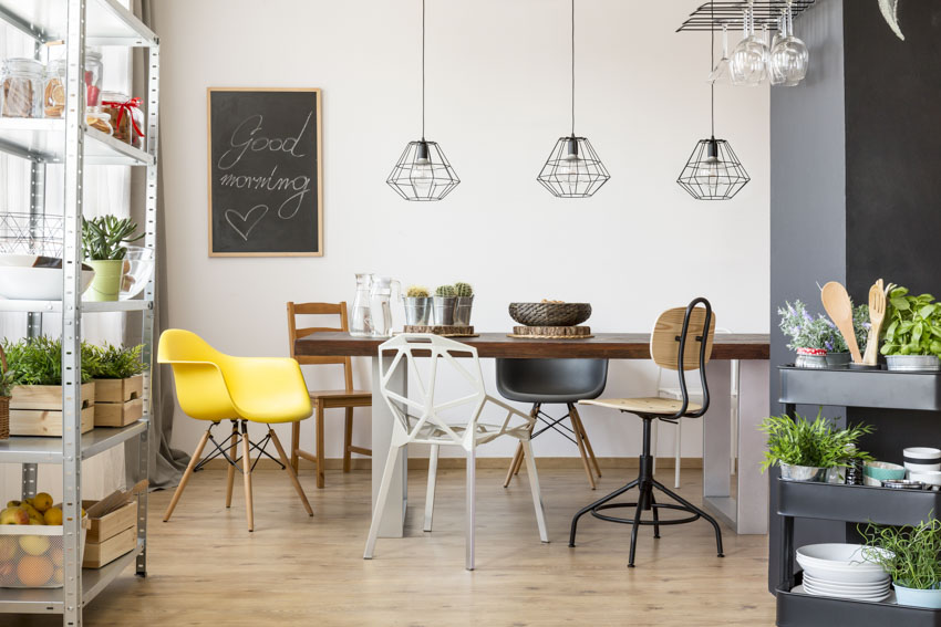 Sala pequeña con mesa, diferentes tipos de sillas decorativas, lámparas colgantes, piso de madera y plantas de interior